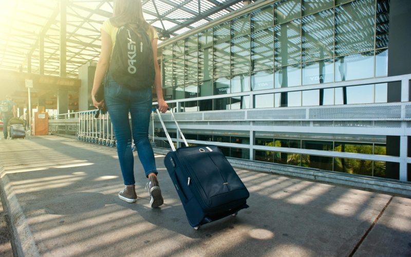 A woman walks with a suitcase outside an airport terminal, ready for travel.