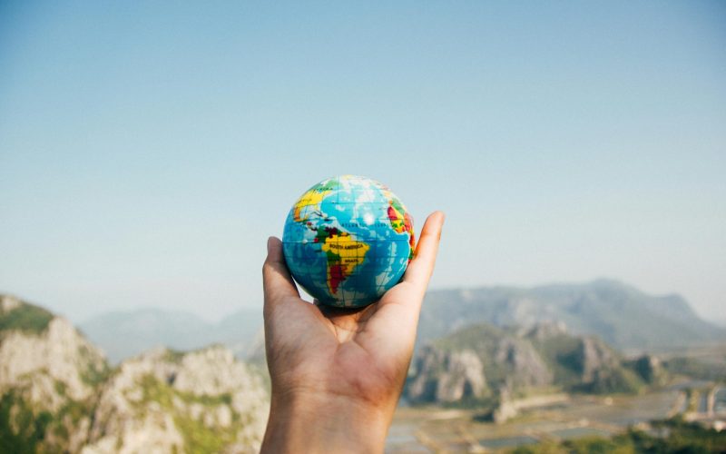 Hand holding a globe against a mountain background symbolizing travel and exploration.